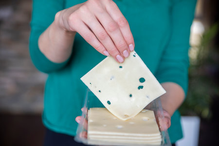 A womans hand takes a piece of cheese from a pack close-up. Preparing for Cheese Lovers Day.