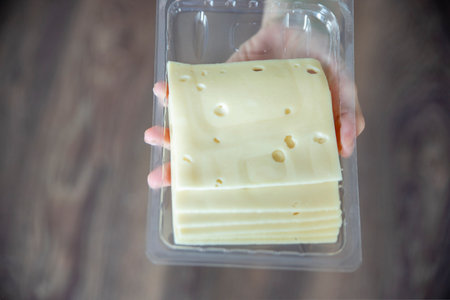 A womans hand takes a piece of cheese from a pack close-up. Preparing for Cheese Lovers Day.