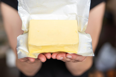 A hand holds butter in a pack close-up. Process of making sandwiches with butter.の写真素材