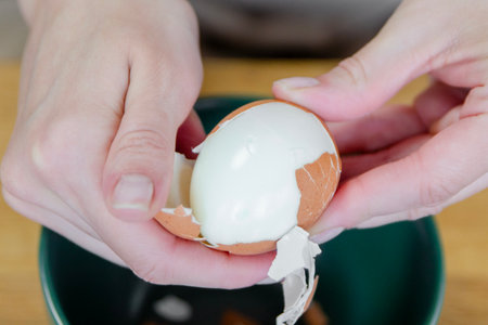A womans hand peels a boiled egg, removing the shell close-up. A quick snack in the form of a boiled egg. Top view.の写真素材
