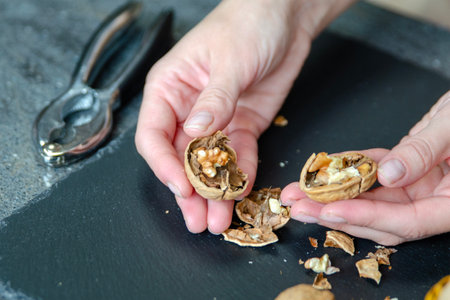 Close-up of a womans hands taking a walnut out of the shell with nutcracker. Snack on healthy nuts. Side view.の写真素材