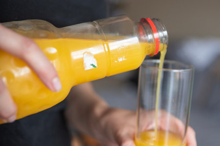A womans hand pours orange juice into a glass. Pouring process into glass.の写真素材