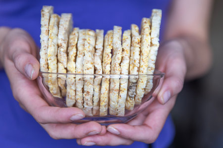 A hand holds a bowl of corn chips close-up. The process of eating a quick snack in the form of corn chips.の写真素材