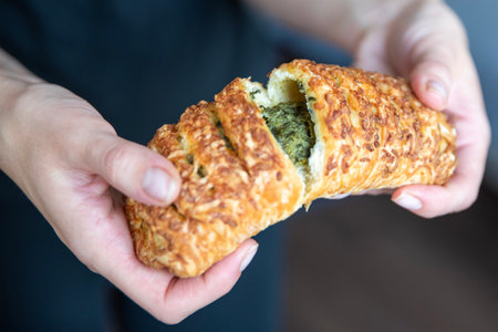A hand breaks a spinach bun in half close-up. Eating quick snacks.
