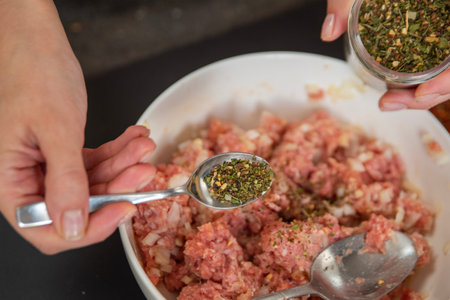 Womans hands pouring seasoning into meat close-up. The process of cooking meat.