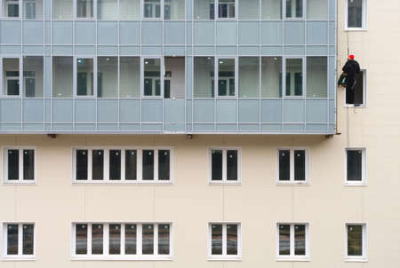 Beige facade of building under construction with many windows and balconies. The alpinist working on the facade suspended on the cord.の写真素材