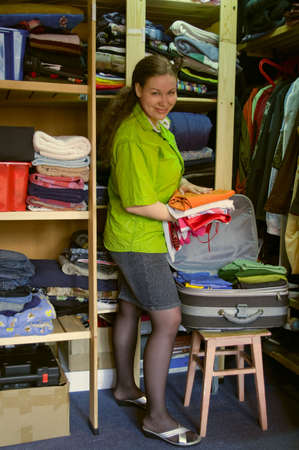 Woman in the wardrobe packs things into a suitcase and smilesの写真素材