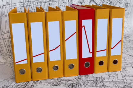 Row from the yellow file folders and one red folder with clean blanks for your text. Red annual line diagram through it. Black and white project drawings are backgroundの写真素材