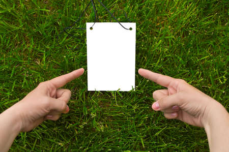 White sheet in woman`s hands for your text. Green grass is background. Two fingers point on noteの写真素材