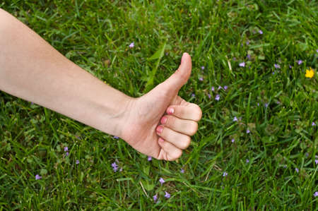 Thumb up in green meadow background. Caucasian woman`s handの写真素材