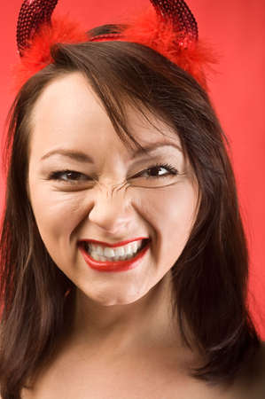 Facial portrait of a beautiful young woman in devils horns on red background. Close up