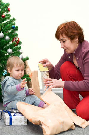 Senior woman and little child are opening gifts in Christmas eve. Fir on backgroundの写真素材