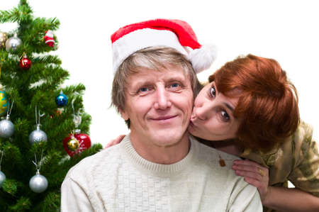 Mature woman kissing a old husband near the Christmas tree. Loving senior couple isolated on white backgroundの写真素材