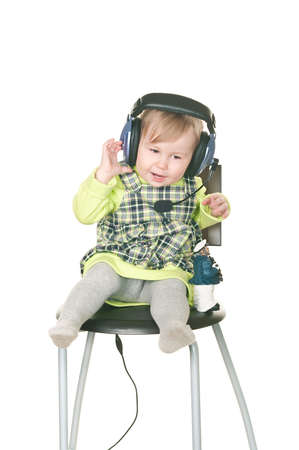 The happy small child sits on a chair in headset ear-phones with a microphone. Isolated on white backgroundの写真素材