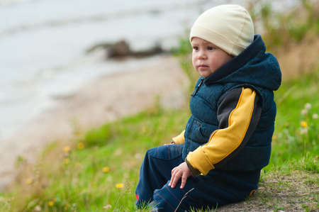 Young boy sitting on the rocks next to a lake lonely. He is in melancholy moodの写真素材