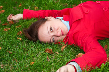 Woman with the yellow leaf lies on the green grass meadow