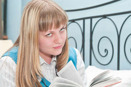 The girl the blonde reads the book lying on a bedの写真素材