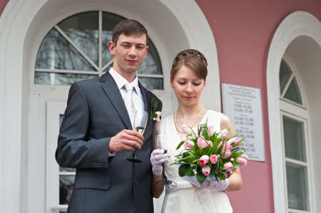 Bride and groom standing near registry office with glasses of champagne. Caucasians. Young wedding coupleの写真素材
