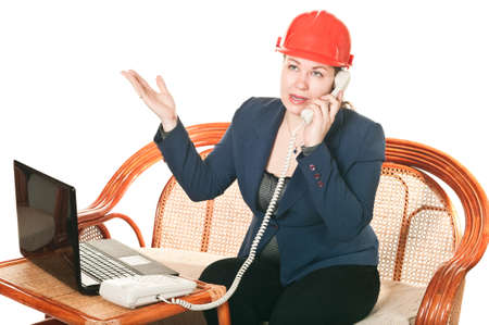 The girl in a red helmet with the laptop sits at a table and calling by phone. Isolated on white backgroundの写真素材