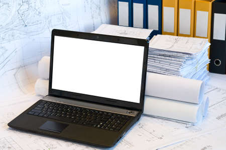 Opened laptop and stack of project drawings. Rolled papers. Working place. White screenの写真素材