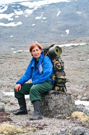Backpacker a mature woman sitting on rock in mountainsの写真素材