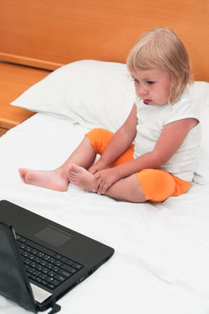 A small child is sitting with a laptop on the bedの写真素材