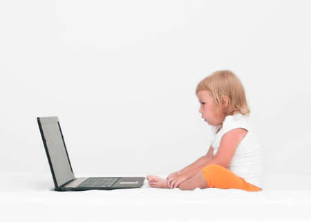 A small child is sitting with a laptop on the bedの写真素材