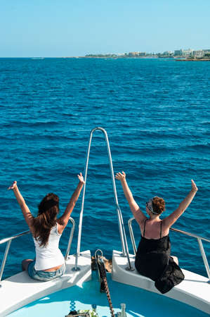 Two women on yacht seating on stern in blue seaの写真素材