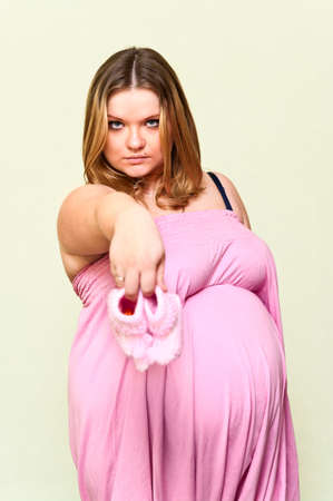 Pregnant young Caucasian woman holding in hands baby`s pink bootee.の写真素材