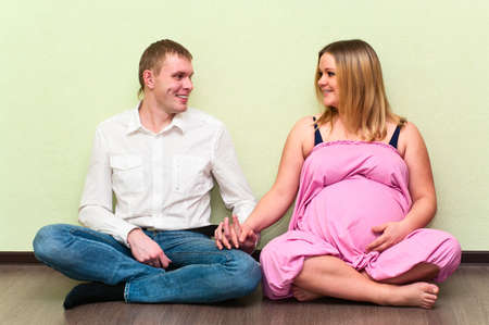 Pregnant woman with her husband sitting on floor in empty room. Caucasians, a loving young coupleの写真素材
