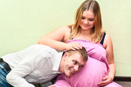Pregnant woman with her husband hearing belly. Caucasians, a loving young coupleの写真素材