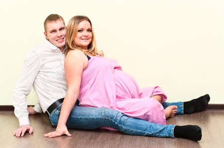 Pregnant woman with her husband sitting on floor in empty room. Caucasians, a loving young coupleの写真素材