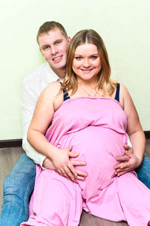 Pregnant woman with her husband sitting on floor in empty room. Caucasians, a loving young coupleの写真素材