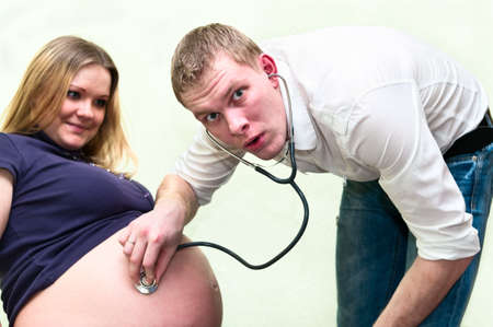 Pregnant woman with her husband listen belly by stethoscope. Caucasians, a loving young coupleの写真素材