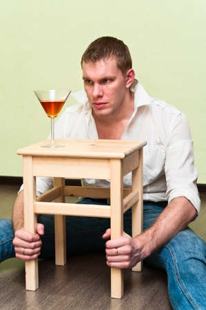 Drunken man sitting on floor with glass of alcohol and holding stoolの写真素材