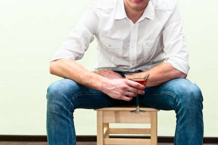 Drunken man sitting on stool with glass of alcohol. Unrecognizable personの写真素材