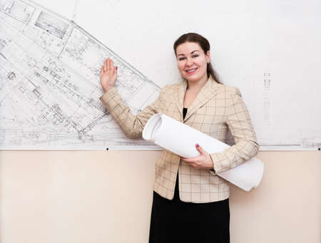 One young woman a architect standin near the big blueprint on wall and showingの写真素材