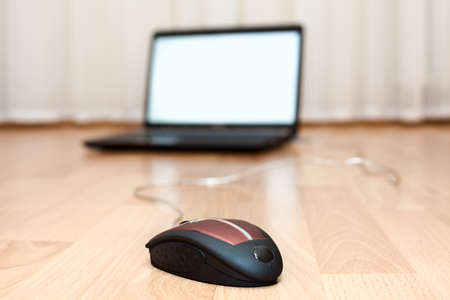Opened laptop and a computer mouse on the floor of the roomの写真素材
