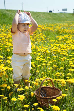 Little child standing on field of flowers with basket and playing in cowの写真素材