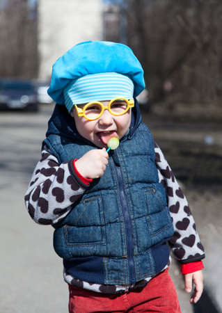 Little child with lollipop is standing outdoors. Funny glasses の写真素材