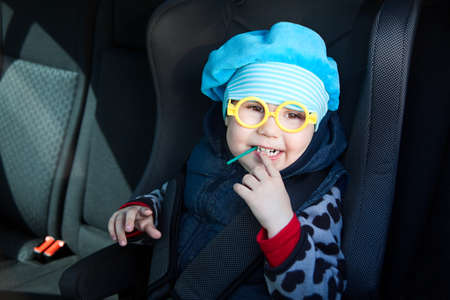 Little child sitting in carseat in vehicle with lollipop. Funny glassesの写真素材