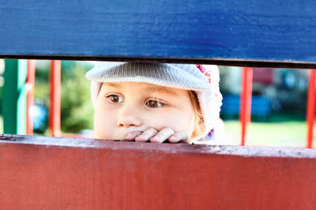 Little child looking through a crack between wooden planks