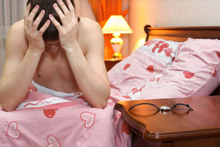 One man in the bed after a heavy hangover. Early morning. Wristwatch on a tableの写真素材