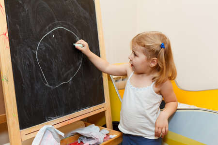One small Caucasian girl drawing with chalk on blackboardの写真素材