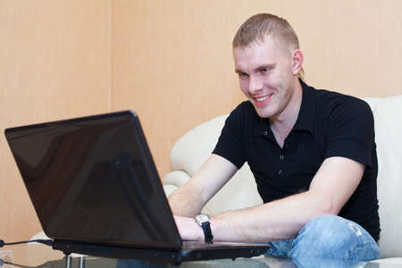 Handsome man playing in games on laptop. Male sits in domestic room interiorの写真素材