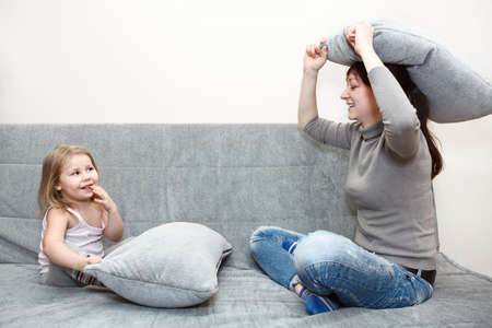 Little child and young mother in pillow fighting on sofaの写真素材
