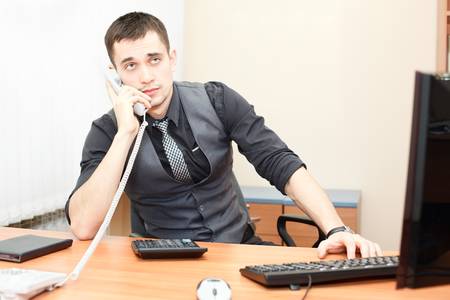 Smart businessman speaking on phone while working on desktop computerの写真素材