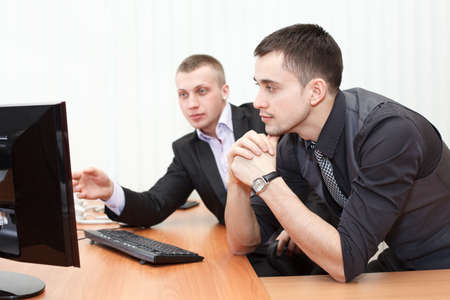 Two business men looking together at computer screen in officeの写真素材
