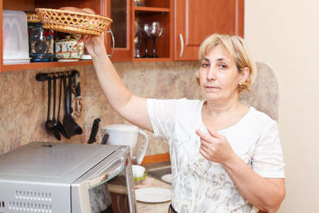 Mature woman standing in kitchen with breadbasketの写真素材