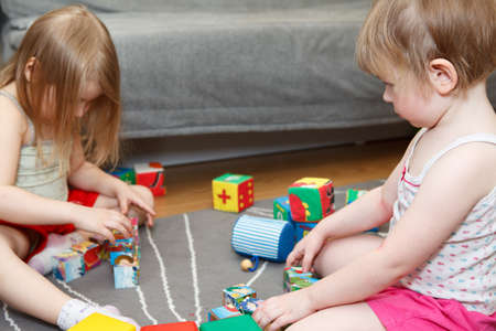 Small girls playing with bricks on floor at domestic roomの写真素材